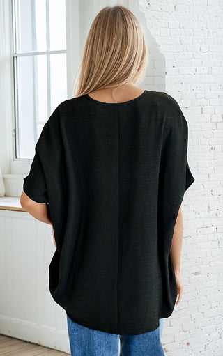 Person wearing a black oversized shirt in a room with white brick walls and a window.