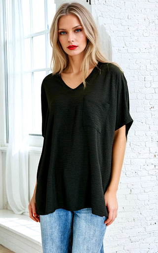 Woman wearing a black oversized t-shirt and blue jeans against a white brick wall.