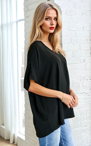 Woman wearing a black oversized top and blue jeans against a white brick wall.