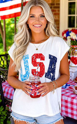 Woman wearing a 'USA' graphic t-shirt, holding a mason jar with a red, white, and blue design, outdoors.