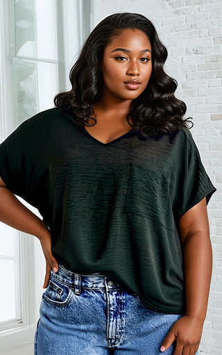 Woman wearing a dark green oversized t-shirt and blue jeans indoors.