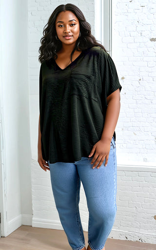 Plus size Woman wearing a black oversized shirt and blue jeans against a white brick wall.