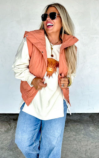 Woman in forward-facing pose wearing Highland Cow embroidered sweatshirt with rust vest and wide leg jeans.