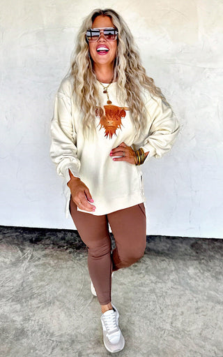 Full-body image of woman in Highland Cow cozy sweatshirt paired with brown leggings and sneakers.