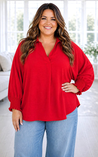 Curvy model wearing a red woven v neck top with long smocked sleeves