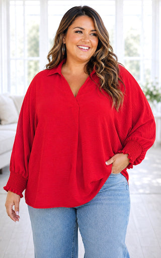 Plus size model wearing a woven red v neck top with long sleeves 