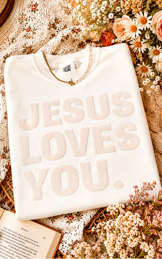 Cream Jesus Loves You Comfort Colors graphic tee with textured lettering styled in a floral cottage flat lay