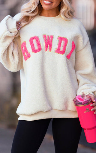 Person wearing a cream sweater with pink text and holding a pink tumbler.