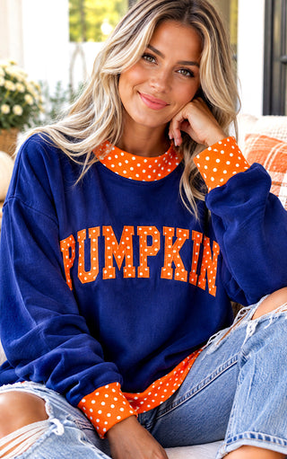 A woman wearing a navy blue sweatshirt with 'PUMPKIN' printed in orange polka-dot letters across the front, paired with distressed blue jeans.