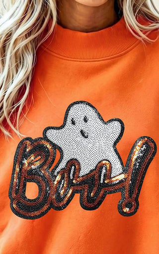 Close-up of a person wearing an orange sweatshirt with a large sequined 'Boo!' graphic and a white ghost motif on the front.