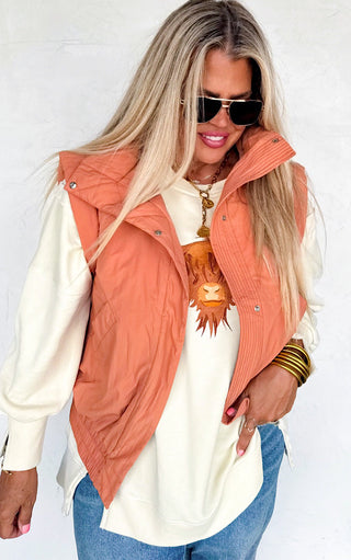 Woman wearing an orange puffer vest over a white shirt with a neutral background