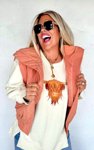 Person wearing a white shirt with a graphic design, peach vest, and sunglasses against a white background