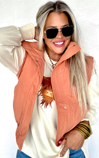 Woman wearing an orange vest over a white top with sunglasses and a neutral background