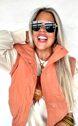 Woman wearing a peach-colored vest and sunglasses against a white background