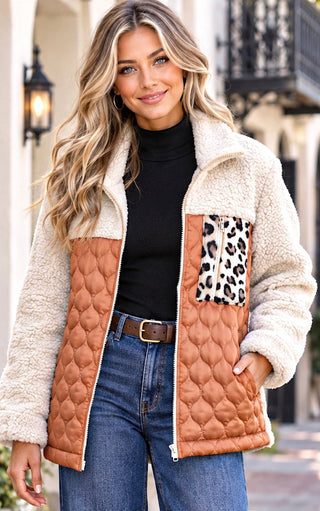 A woman wearing a color block jacket with a cream sherpa fleece collar and sleeves, a quilted tan-brown body, and a leopard-print pocket panel, styled with a black turtleneck and blue jeans.