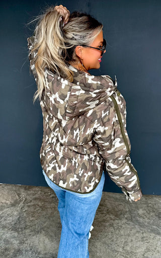 Person wearing a camouflage jacket and blue jeans against a dark background