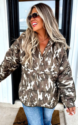 Woman wearing a camouflage jacket with sunglasses and a white wall background