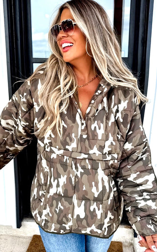 Woman wearing a camouflage jacket and sunglasses indoors.