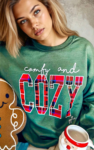 Person wearing a green sweatshirt with 'comfy and cozy' text, sitting next to a gingerbread man and mug.