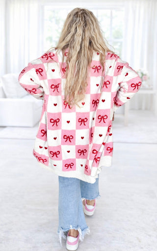 Back view of Person wearing a pink and white checkered cardigan with red bows and hearts.