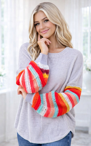 Woman wearing a gray sweater with colorful striped sleeves indoors.