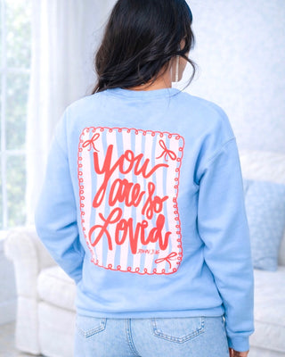 Light blue sweatshirt with red text 'You are so loved' on the back, worn by a person indoors.