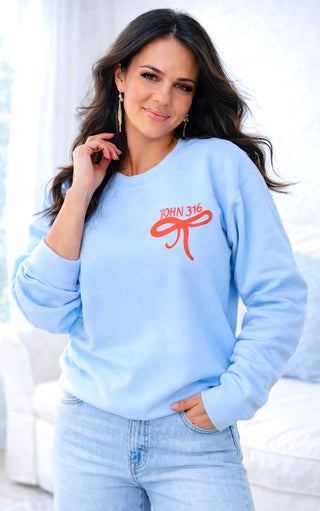 Woman wearing a light blue sweatshirt with a red bow design and 'JOHN 3:16' text.