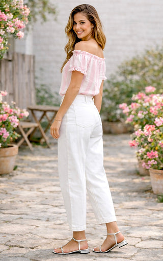 Woman in a pink off-shoulder top and white pants standing in a garden with flowers.