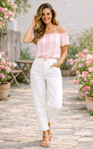 Woman wearing a pink off-shoulder top and white Judy Blue barrel cut jeans in a garden setting
