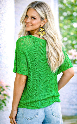 Back view of a woman wearing a green knitted top  with a blurred outdoor background