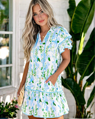 Model wearing feminine blue floral shift dress with flutter sleeves and ruffle hem.