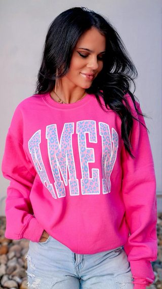 Woman wearing a bright pink sweatshirt with 'AMEN' in leopard print, standing against a neutral background.