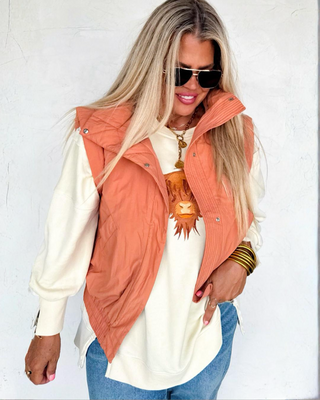 Woman wearing a white sweatshirt with a highland cow design, blue jeans, and an orange vest against a white background.