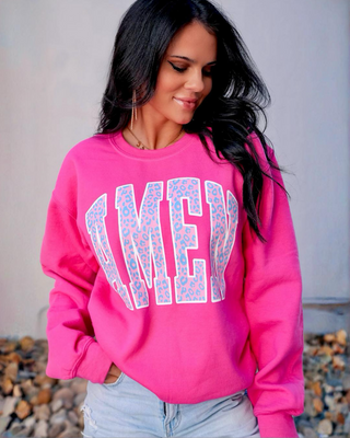 Woman wearing a pink sweatshirt with 'AMEN' printed on it, standing outdoors.