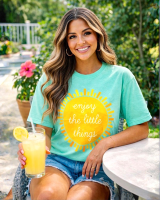 Woman wearing a mint green t-shirt with a yellow sun graphic and text, sitting outdoors.