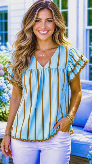 Video of a model in light blue and brown striped flutter sleeve top with white jeans outdoors.