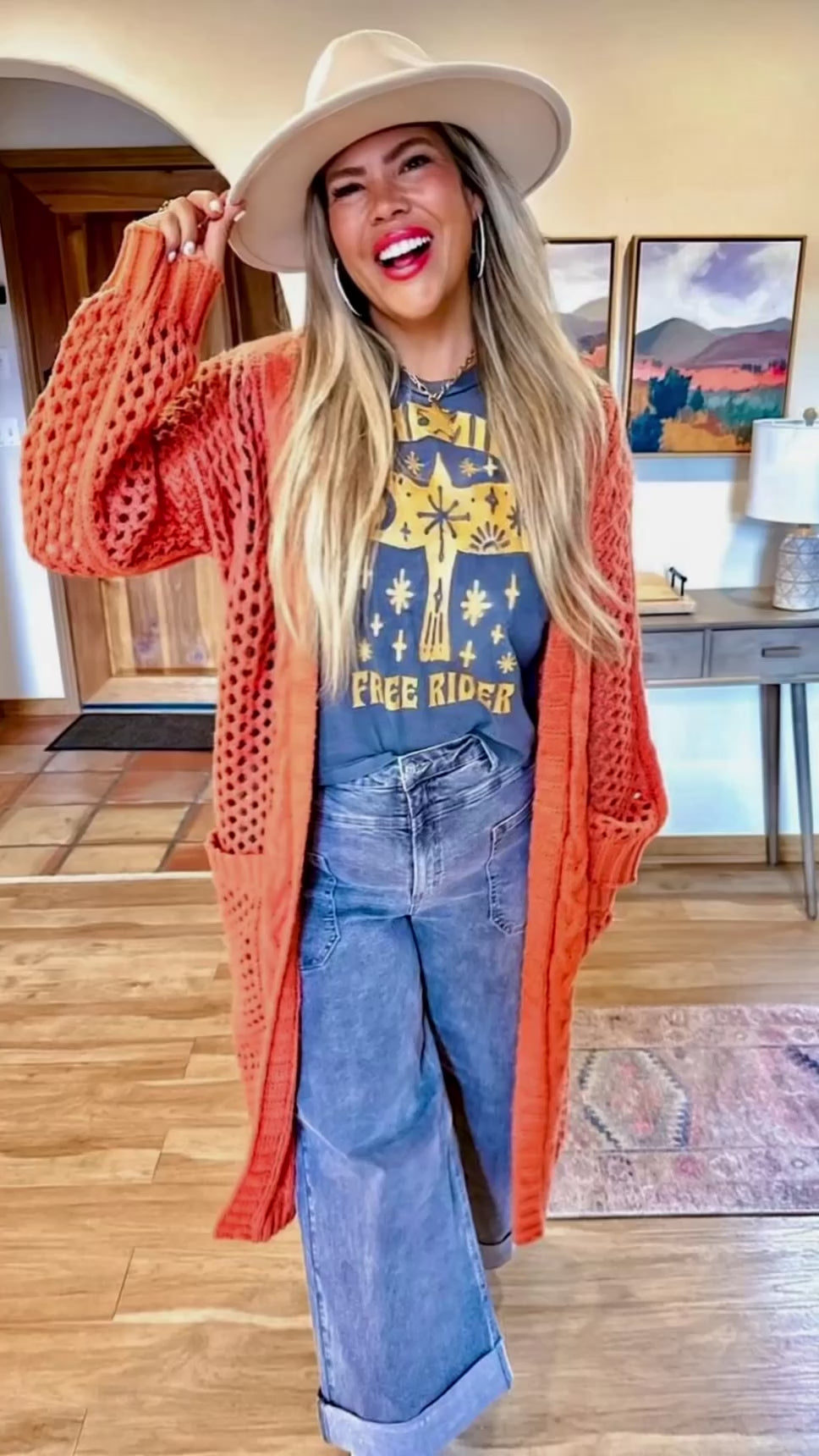 Video of a Woman wearing a rust coral cardigan, graphic t-shirt, and cropped jeans 