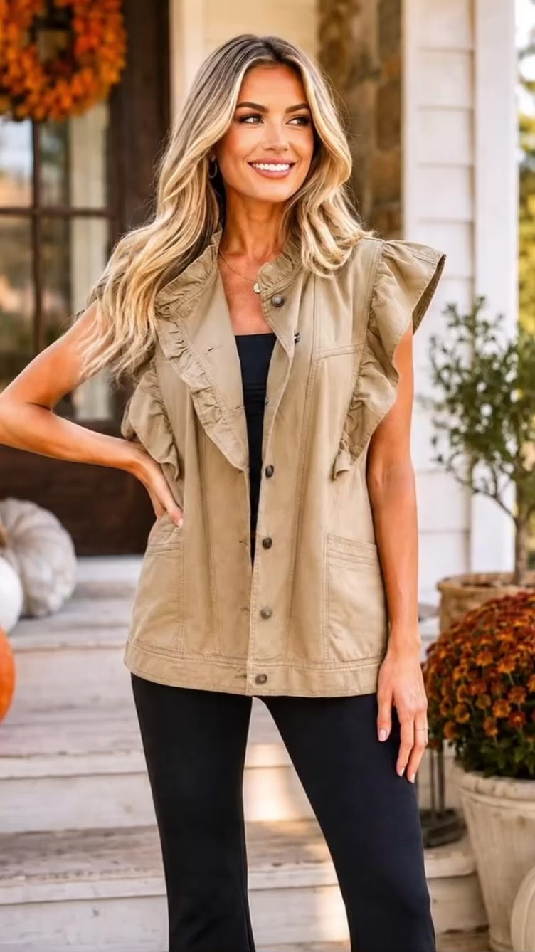 Video of A woman wearing a tan ruffle sleeve utility vest over a white top and black leggings , standing in front of a house porch.
