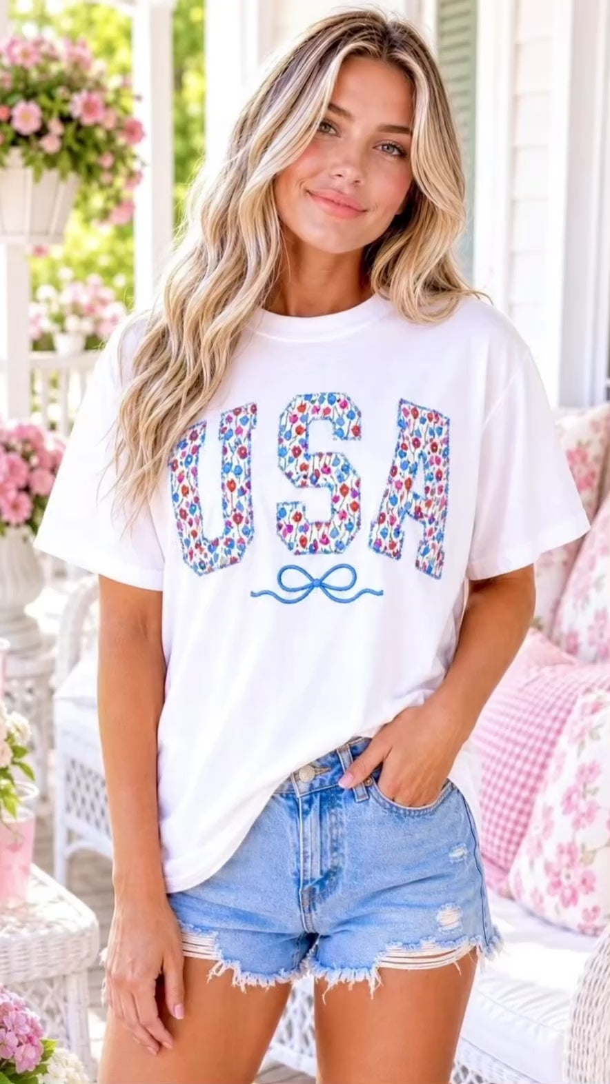 Video of blonde model wearing a USA patches embroidered comfort colors tshirt in shades of light blue, red and pink on a white tee on a southern cottage style front porch