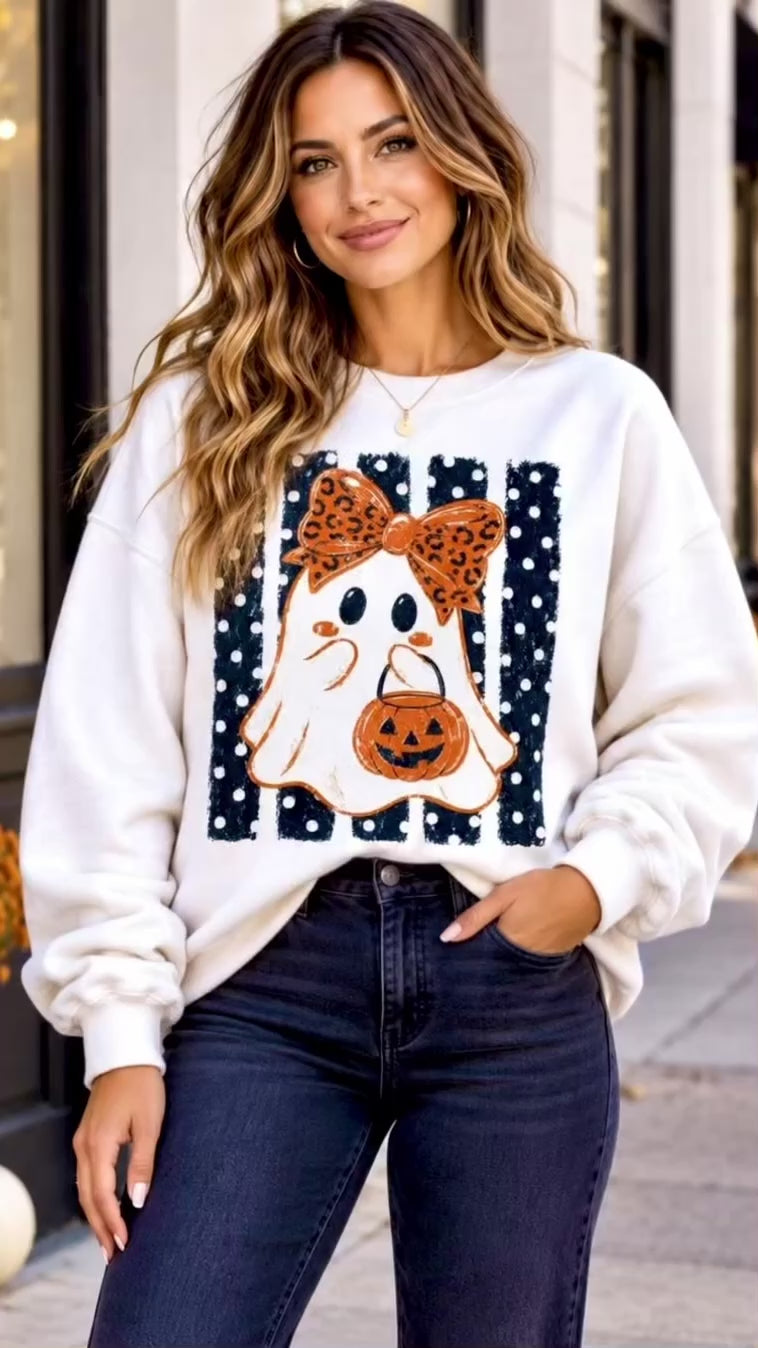 Video of A woman wearing a white graphic sweatshirt with a polka dot Halloween ghost design, paired with black jeans.