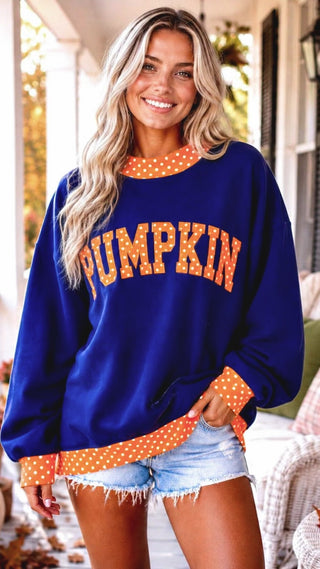 Video of a Woman wearing a navy blue fall sweatshirt with orange polka dot PUMPKIN appliqué, distressed jeans, and a bright autumn porch background.
