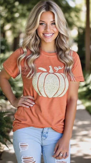Video of a woman wearing an orange colored Comfort Colors tee with a glitter puff print pumpkin design with distressed light-wash jeans.