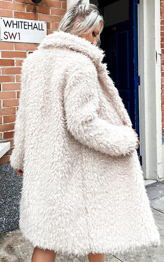 Back view of Female with ash blonde hair wearing long off white faux fur coat  